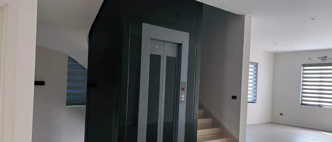Thang máy gia đình kính và inox đặt trong phòng khách nhiều ánh sáng tự nhiên